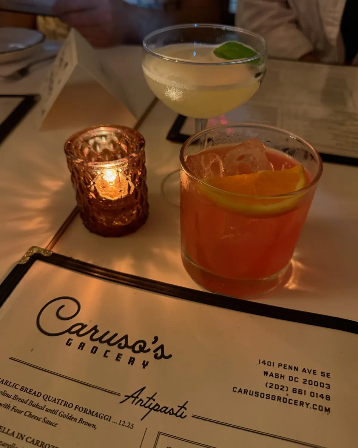 Two cocktails and a candle on a table beside a restaurant menu.
